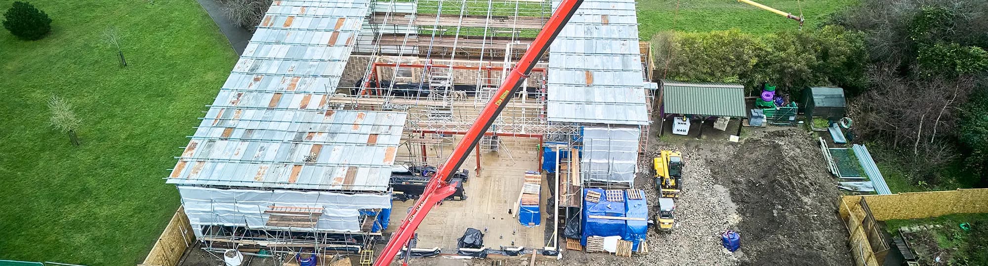 Aerial drone view of a construction site with scaffolded buildings, a crane and an excavator among building materials