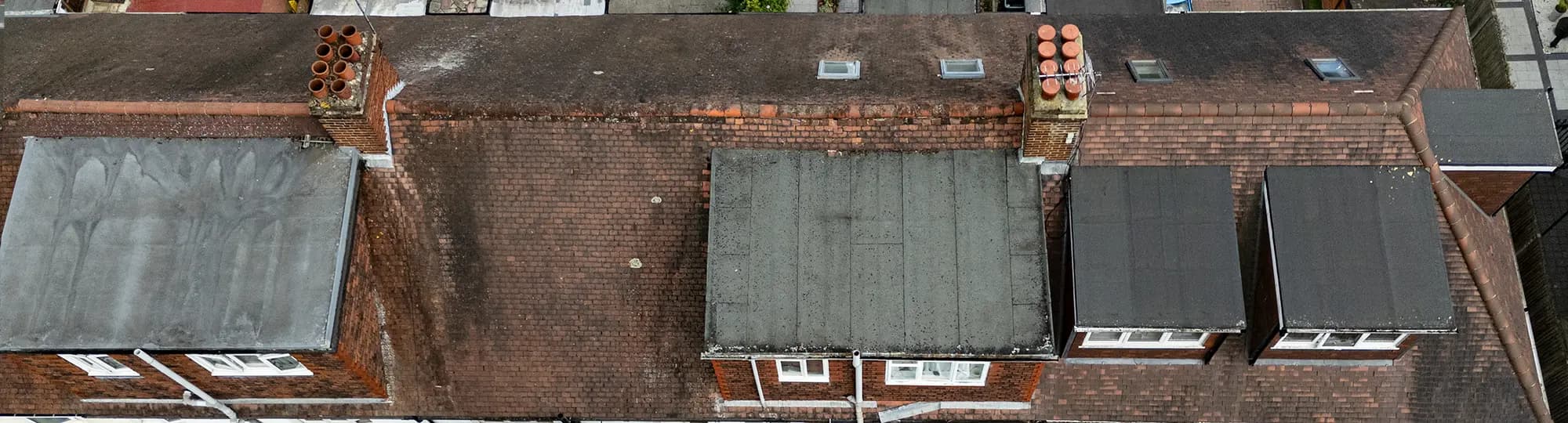 Aerial top-down view of terraced house rooftops with tiled slopes, flat roof dormers and brick chimney stacks